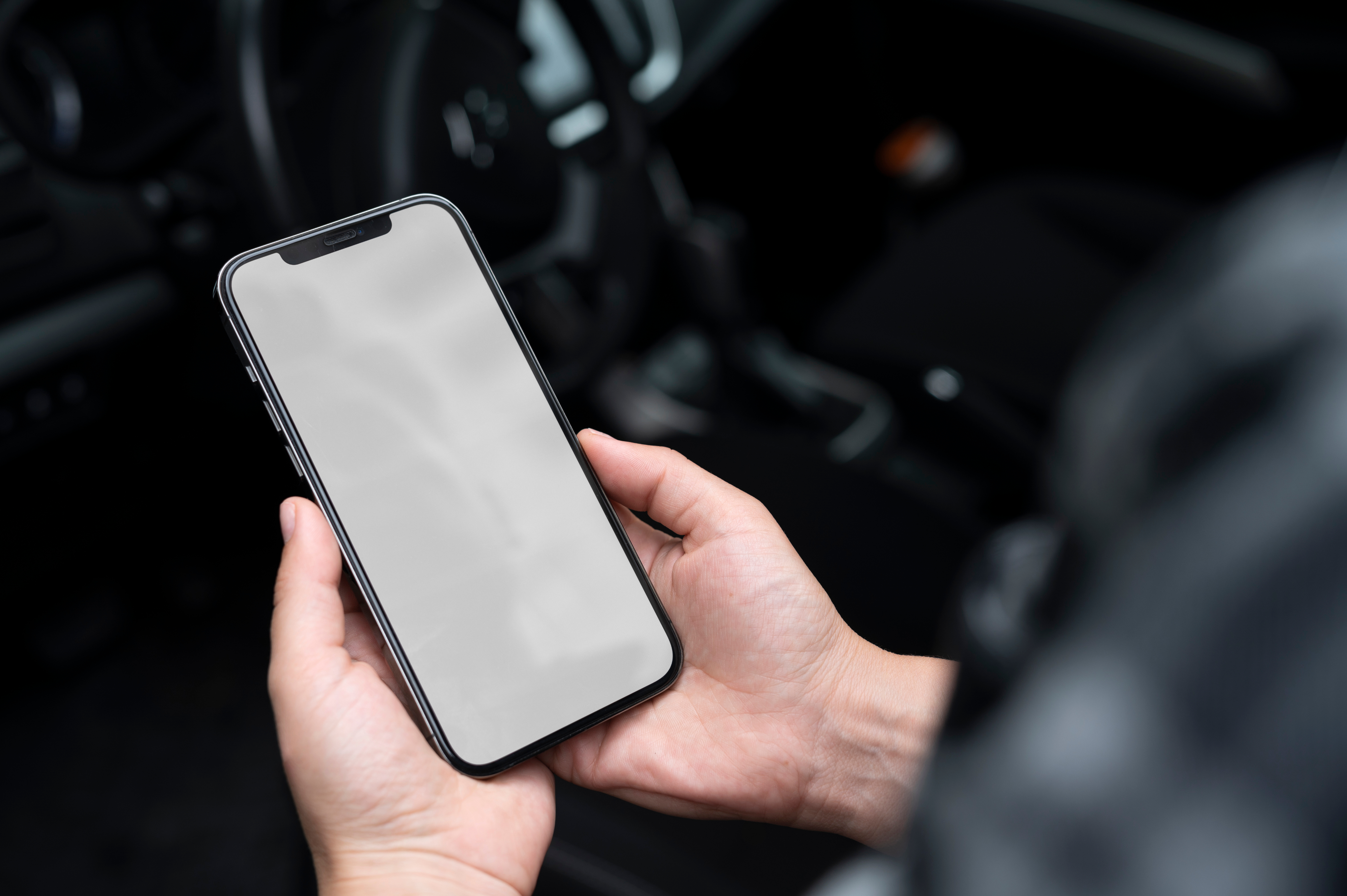 Osoba trzymająca smartfona z pustym ekranem w kabinie samochodu. W tle widać detale wnętrza auta, co sugeruje wygodne otoczenie do korzystania z technologii mobilnej. Idealna ilustracja nowoczesnych rozwiązań w codziennym życiu, związana z producentami myjni bezdotykowych.