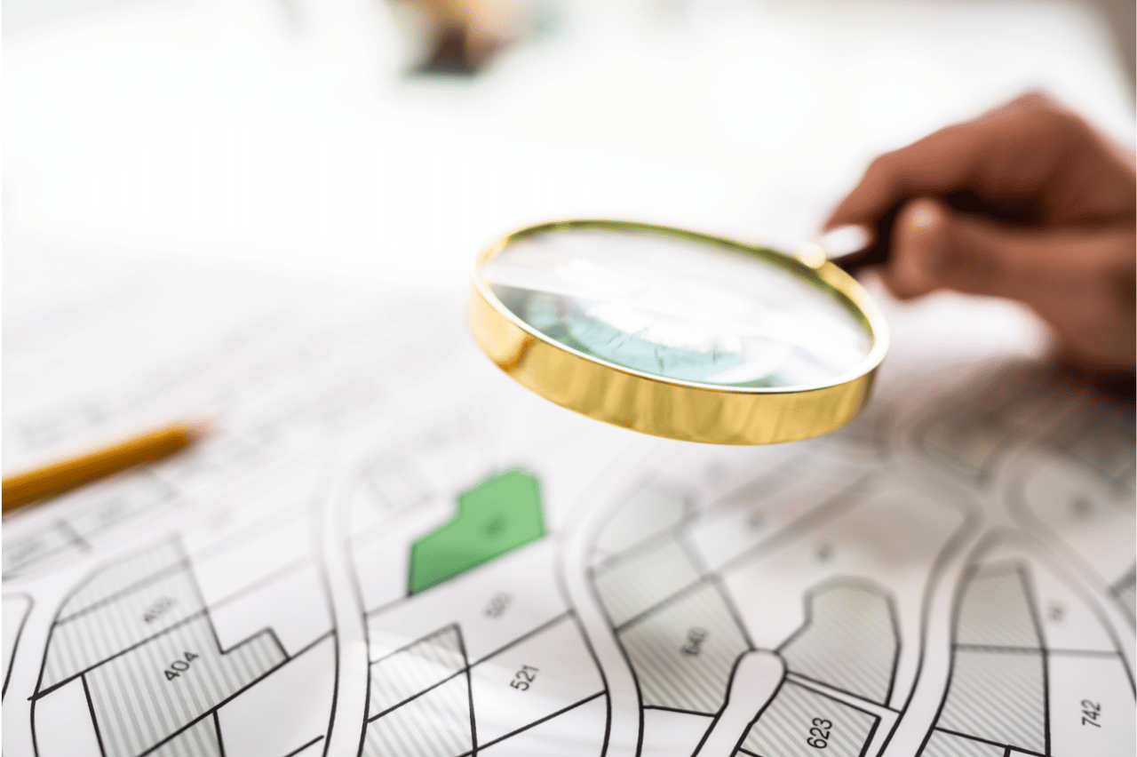 Osoba badająca szczegóły mapy za pomocą szkła powiększającego. Oznaczone obszary na mapie podkreślają dokładność analizy lokalizacji, co może być przydatne dla producentów myjni bezdotykowych.
